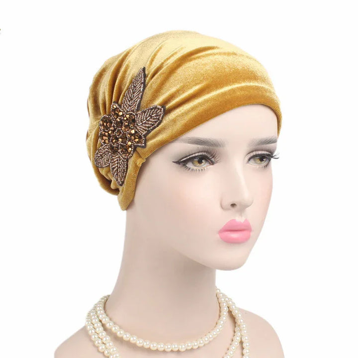 Mannequin wearing a mustard velvet turban with a decorative brown jeweled floral applique and layered pearl necklace