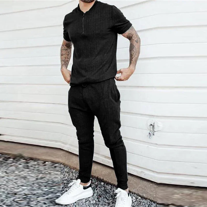 Man wearing black casual jogger pants and black polo shirt with white sneakers against white wall