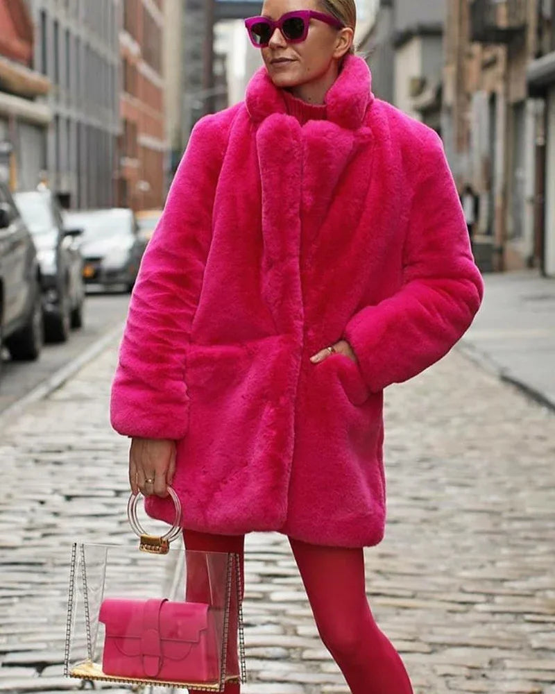 Woman wearing bright pink faux fur coat and sunglasses, holding clear handbag with pink purse on city street