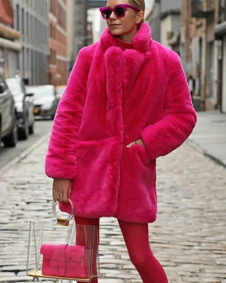 Woman wearing bright pink faux fur coat and sunglasses, holding clear handbag with pink purse on city street