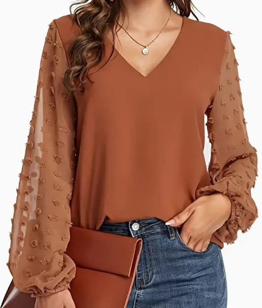 Woman wearing brown blouse with sheer textured puff sleeves paired with blue jeans and holding a matching brown clutch