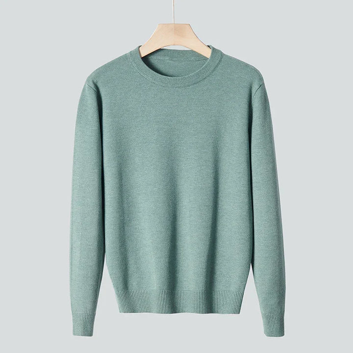 Soft green crew neck sweater hanging on wooden hanger against gray background