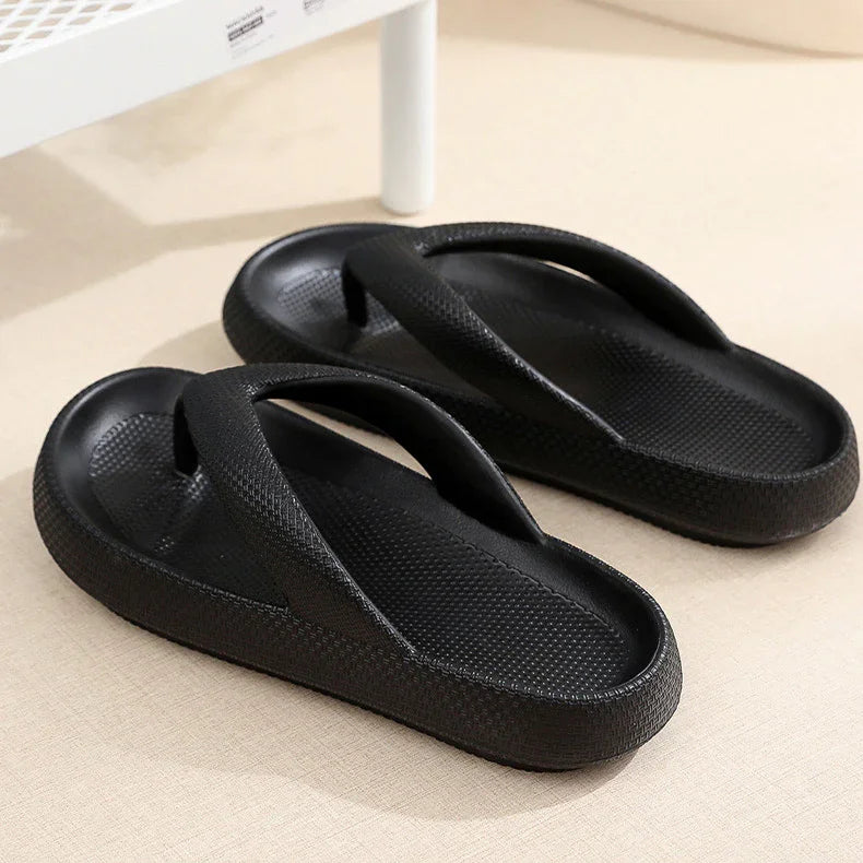Pair of black foam flip-flop sandals with textured straps on beige surface