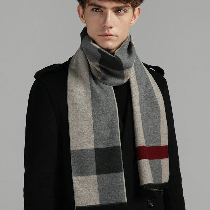 Young man wearing black coat and grey checkered wool scarf with red stripe against grey background