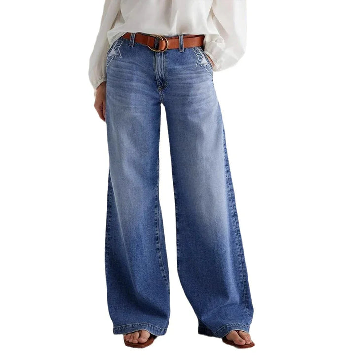 Wide-leg blue denim jeans with star embroidery, brown belt, white blouse, and brown sandals