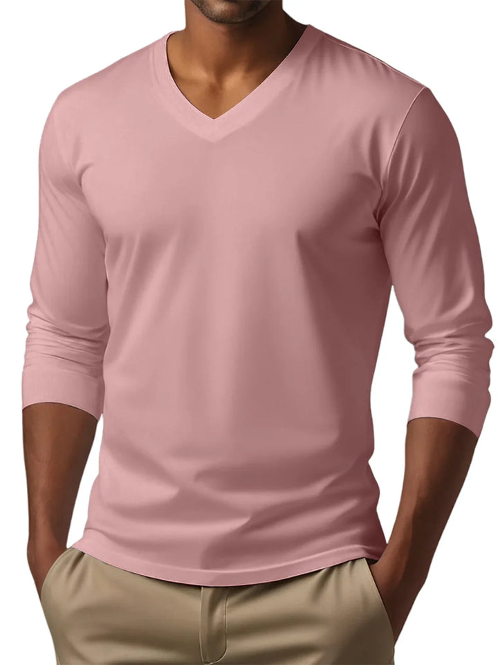 Man wearing a pink long-sleeve V-neck shirt with beige pants against a white background