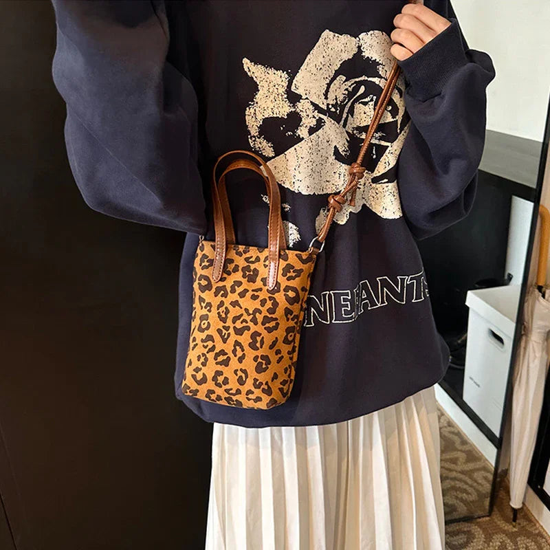Woman wearing black graphic sweatshirt and white pleated skirt holding small leopard print crossbody bag