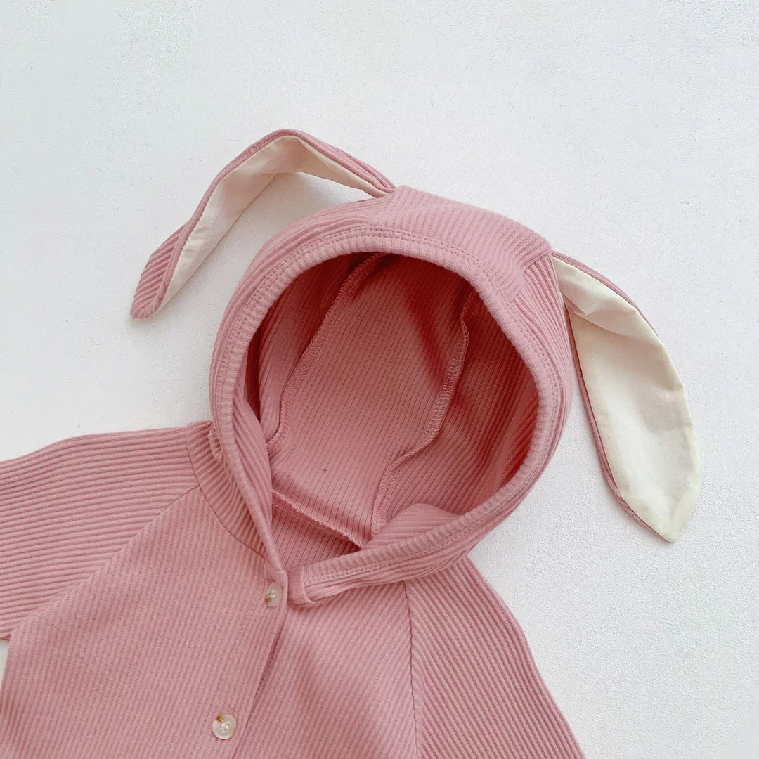Pink ribbed baby romper with hood featuring white inner-lined bunny ears on white background