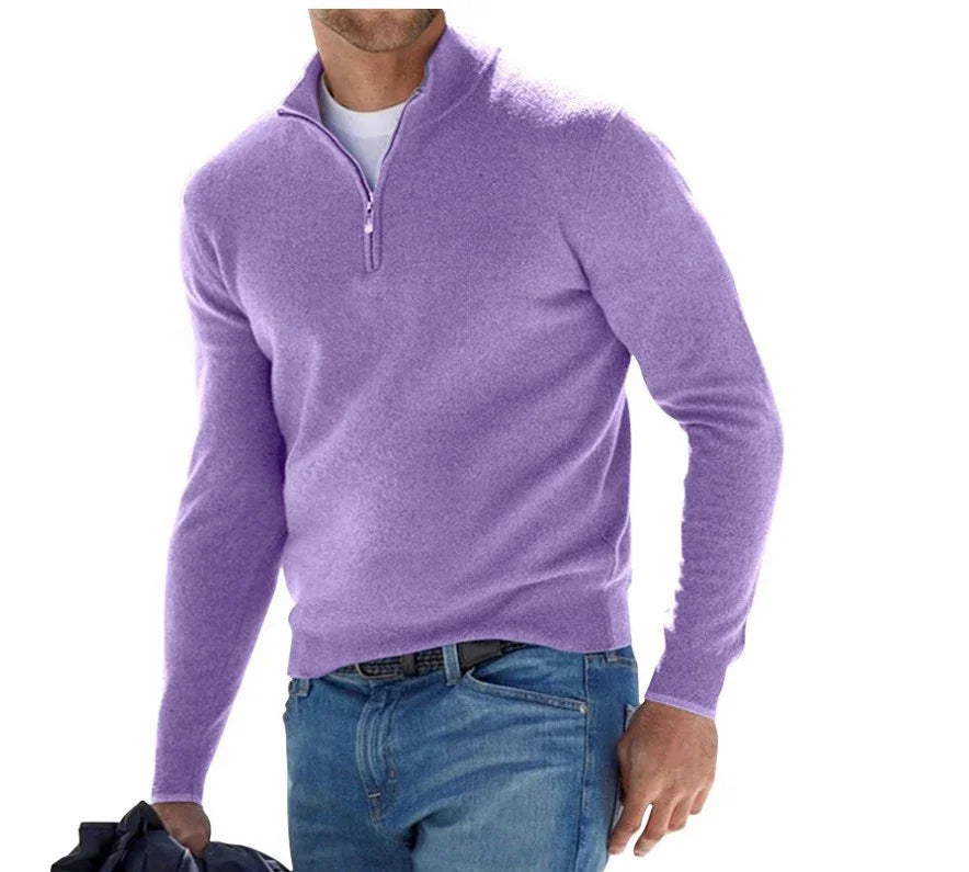 Man wearing a lavender half-zip sweater over a white shirt with blue jeans holding a dark jacket