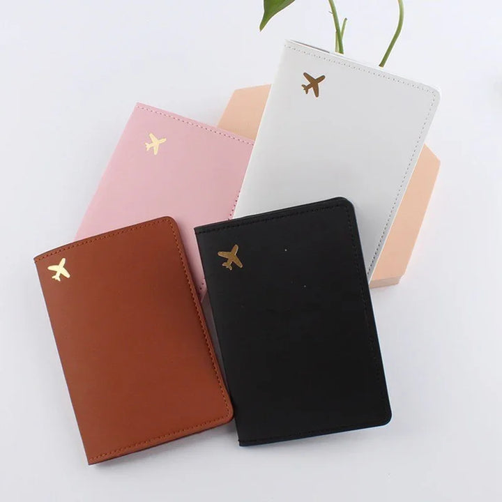 Set of four leather passport holders in pink, white, brown, and black with gold airplane icons