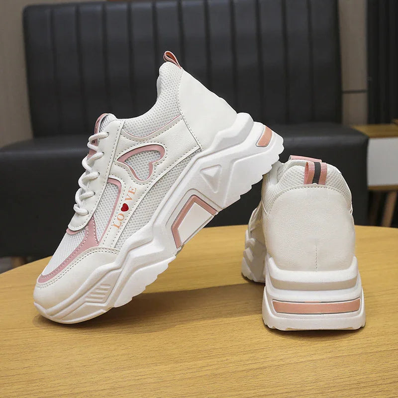 White chunky sneakers with pink heart cutout and LOVE text, displayed on wooden table