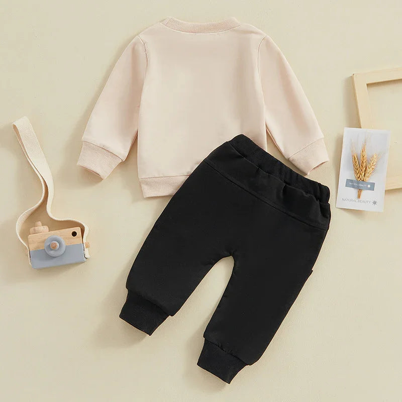 Minimalist toddler outfit with beige long-sleeve top and black elastic waist pants on cream background