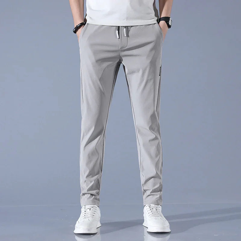 Man wearing light gray casual jogger pants and white sneakers against gray background