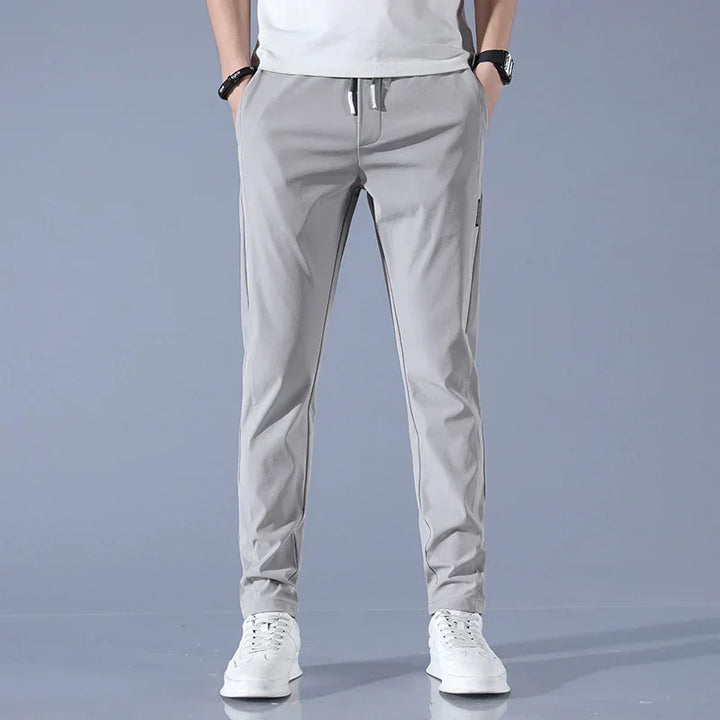 Man wearing light gray casual jogger pants and white sneakers against gray background