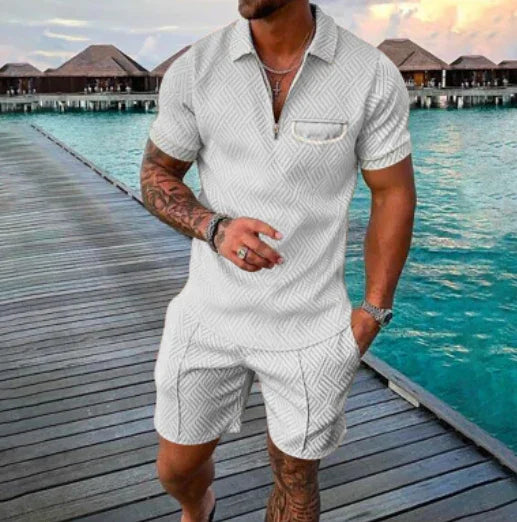 Man wearing white textured short-sleeve polo shirt and matching shorts on wooden dock by turquoise water with overwater bungalows