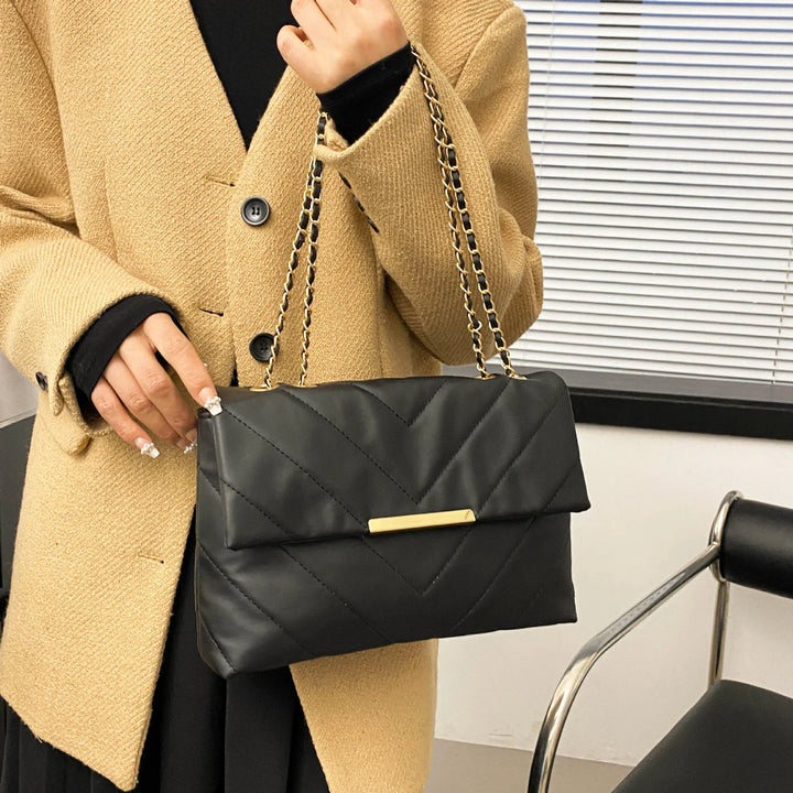 Woman in beige coat holding black quilted leather handbag with gold chain strap
