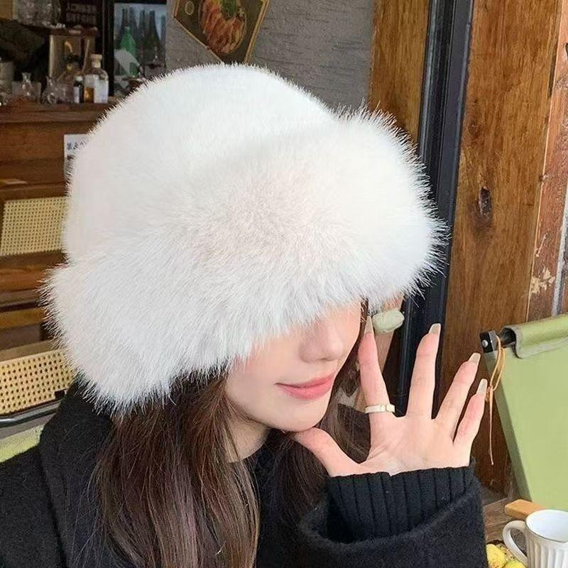 Woman wearing a fluffy white fur hat and black sweater indoors near wooden wall and green chair