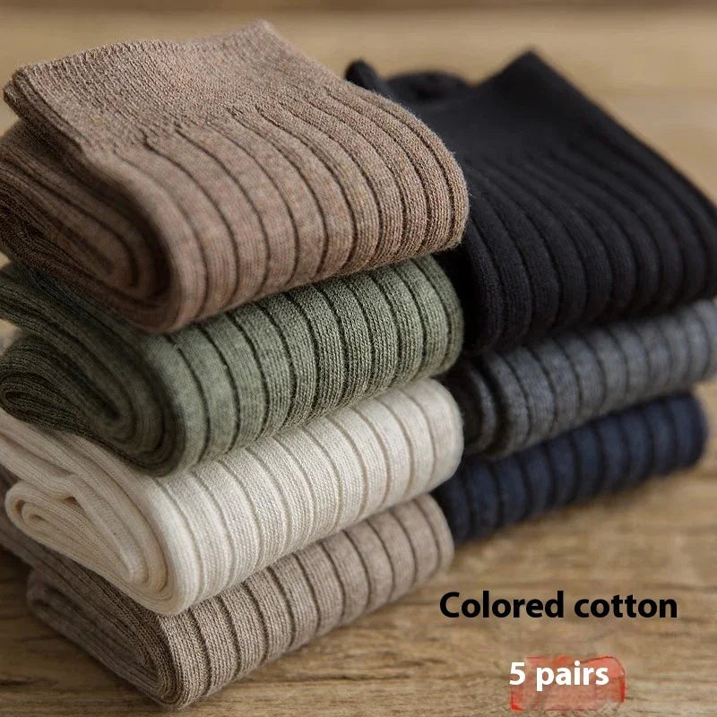 Stack of six pairs of ribbed cotton socks in brown, green, white, beige, black, and gray on wooden surface