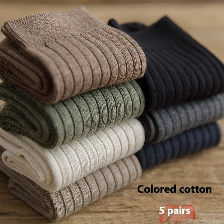 Stack of six pairs of ribbed cotton socks in brown, green, white, beige, black, and gray on wooden surface