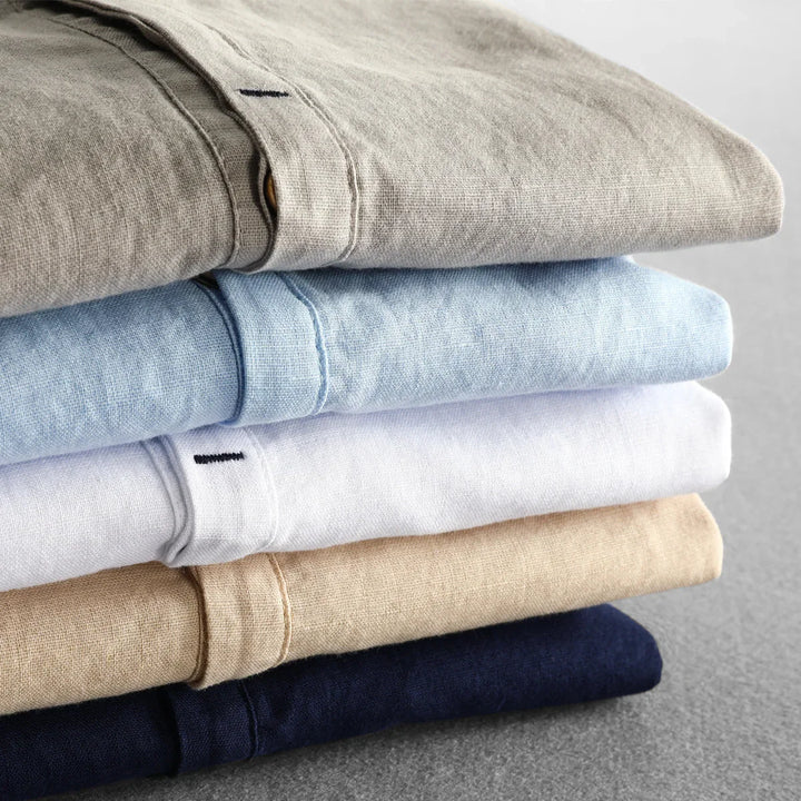 Stack of folded linen shirts in beige, light blue, white, tan, and navy on gray surface