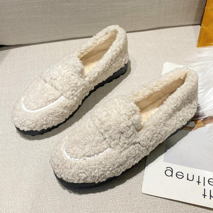 Pair of beige sherpa fleece loafers with black soles on light fabric surface