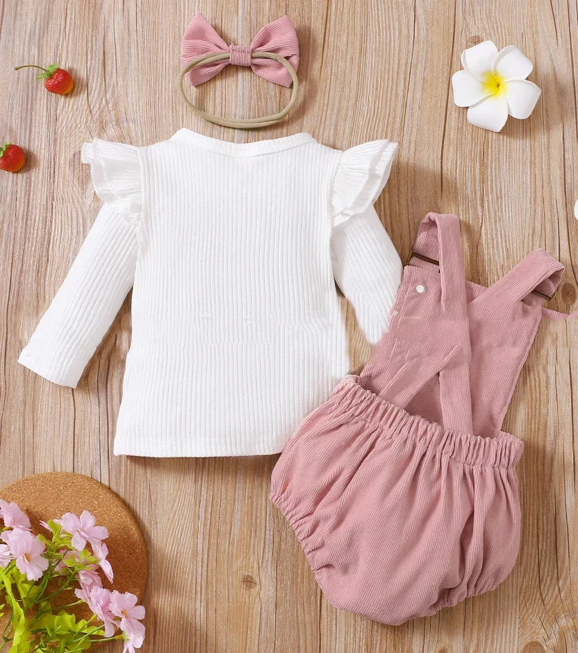 Baby girl outfit with white ruffled long-sleeve top, pink corduroy suspender shorts, and matching pink bow headband