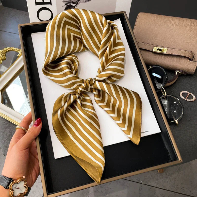 Gold and white striped silk scarf in black box display, styled with sunglasses and beige purse