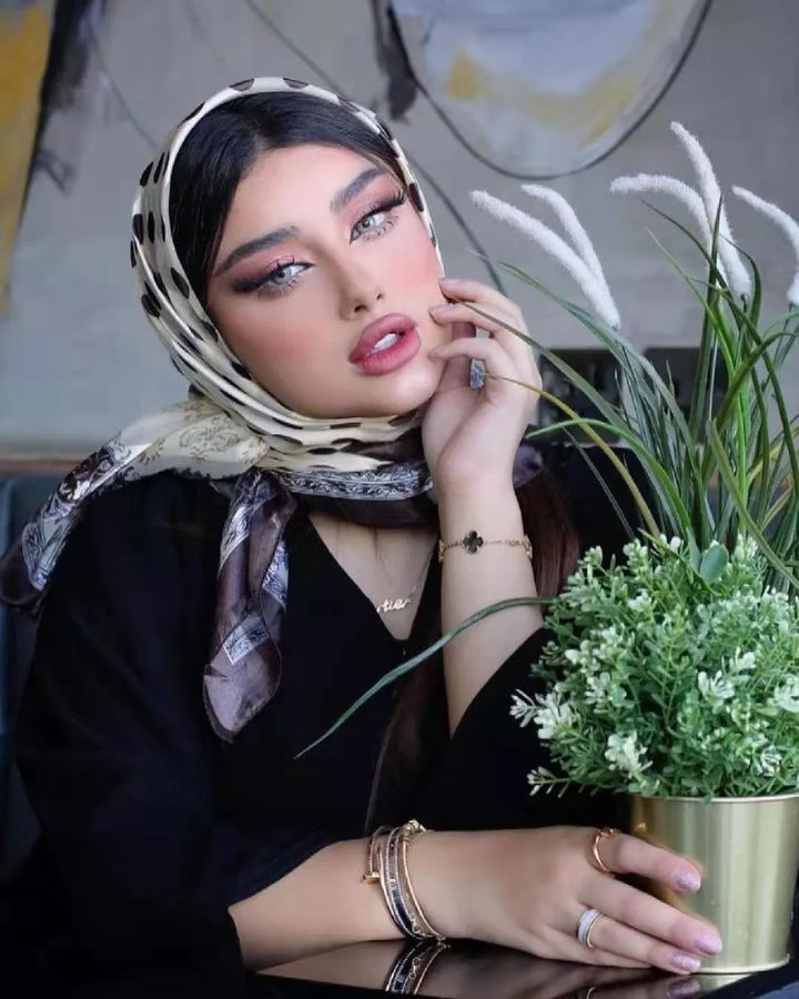 Woman in a polka dot headscarf with bold makeup posing beside green potted plant indoors