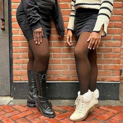 Two women wearing black sheer tights with black combat boots and white fur-lined boots against brick wall