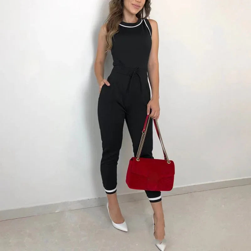 Woman wearing a black jumpsuit with white trim holding a red handbag and white heels