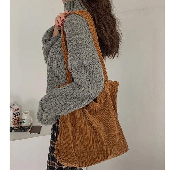 Woman wearing gray knit sweater carrying large brown corduroy tote bag over shoulder