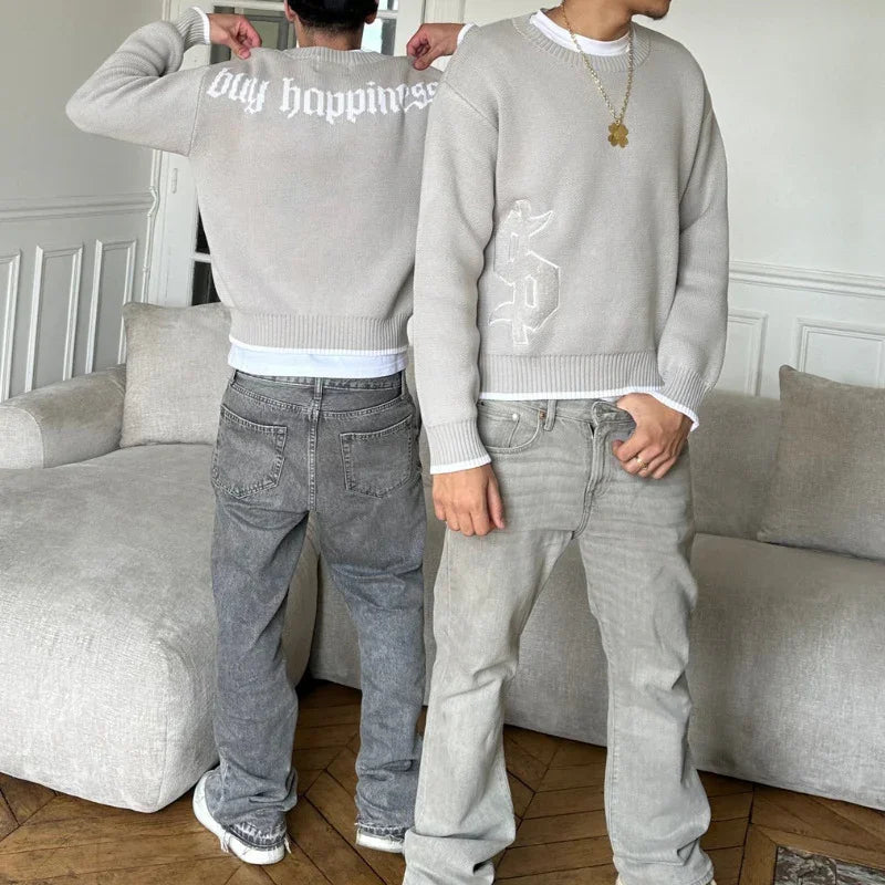 Two men wearing light gray sweaters with white lettering styled with casual gray jeans in a modern living room