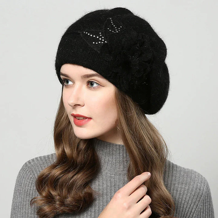 Woman wearing black wool beret with rhinestone detail and flower accent, paired with gray ribbed sweater