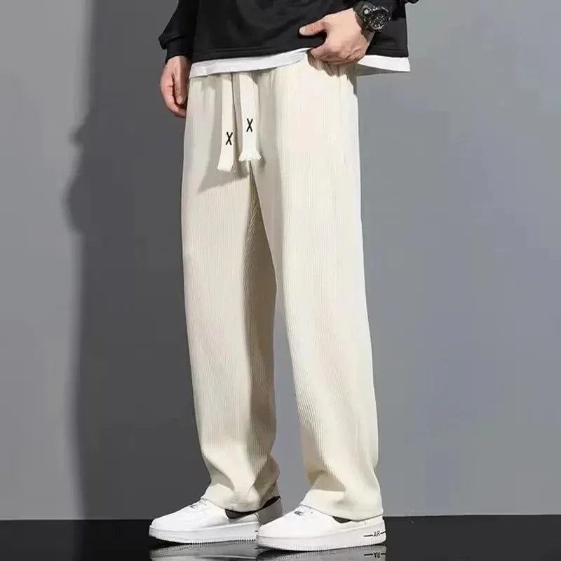Casual cream-colored ribbed pants with drawstring and white sneakers on model against gray background