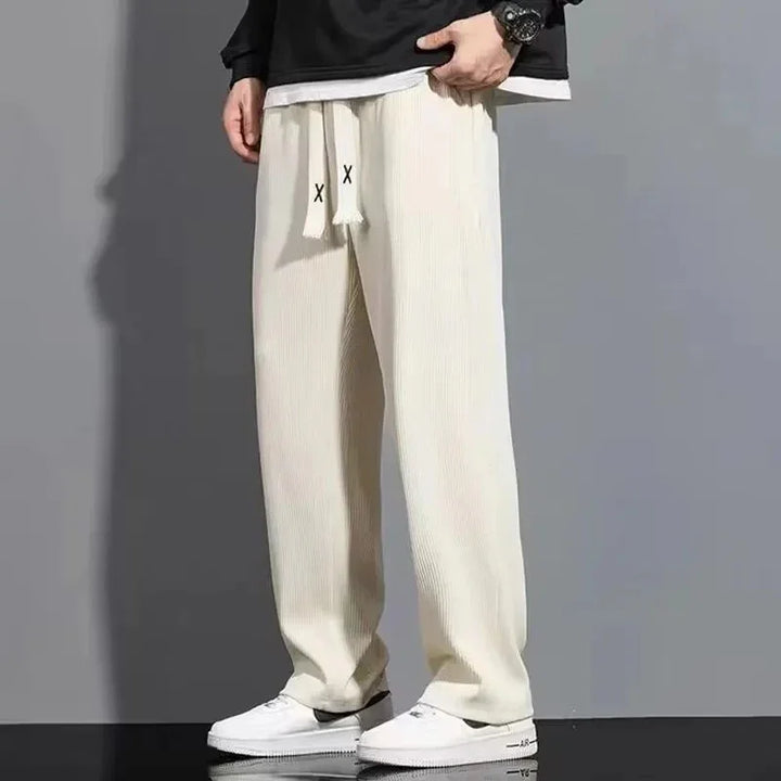 Men's beige ribbed wide-leg pants with drawstring and white sneakers on gray background