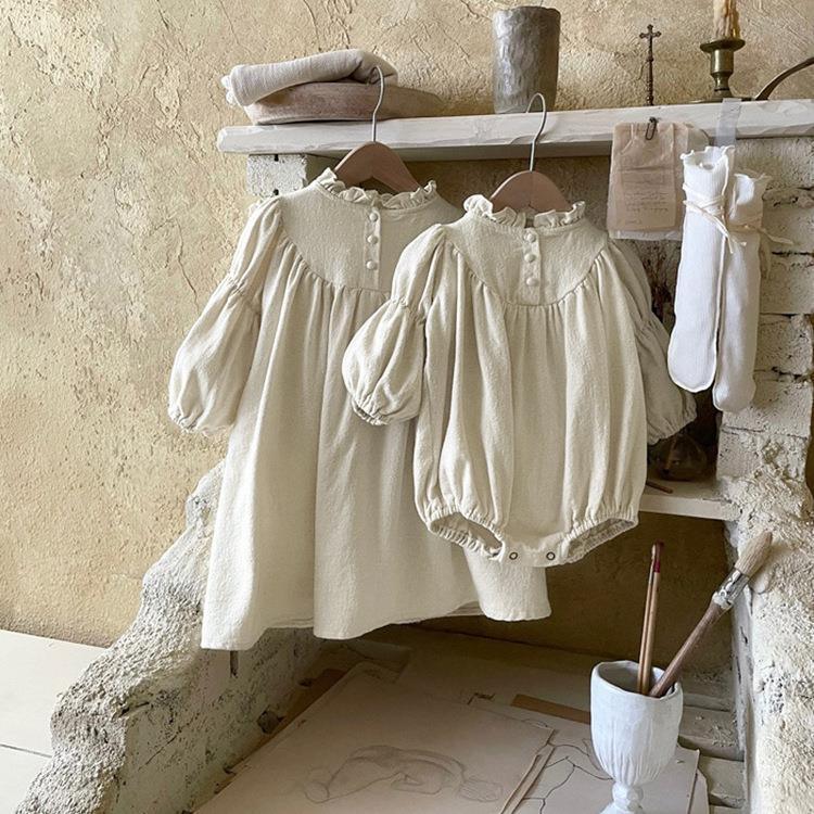 Vintage-style cream baby romper and dress with puff sleeves hanging on a rustic white shelf