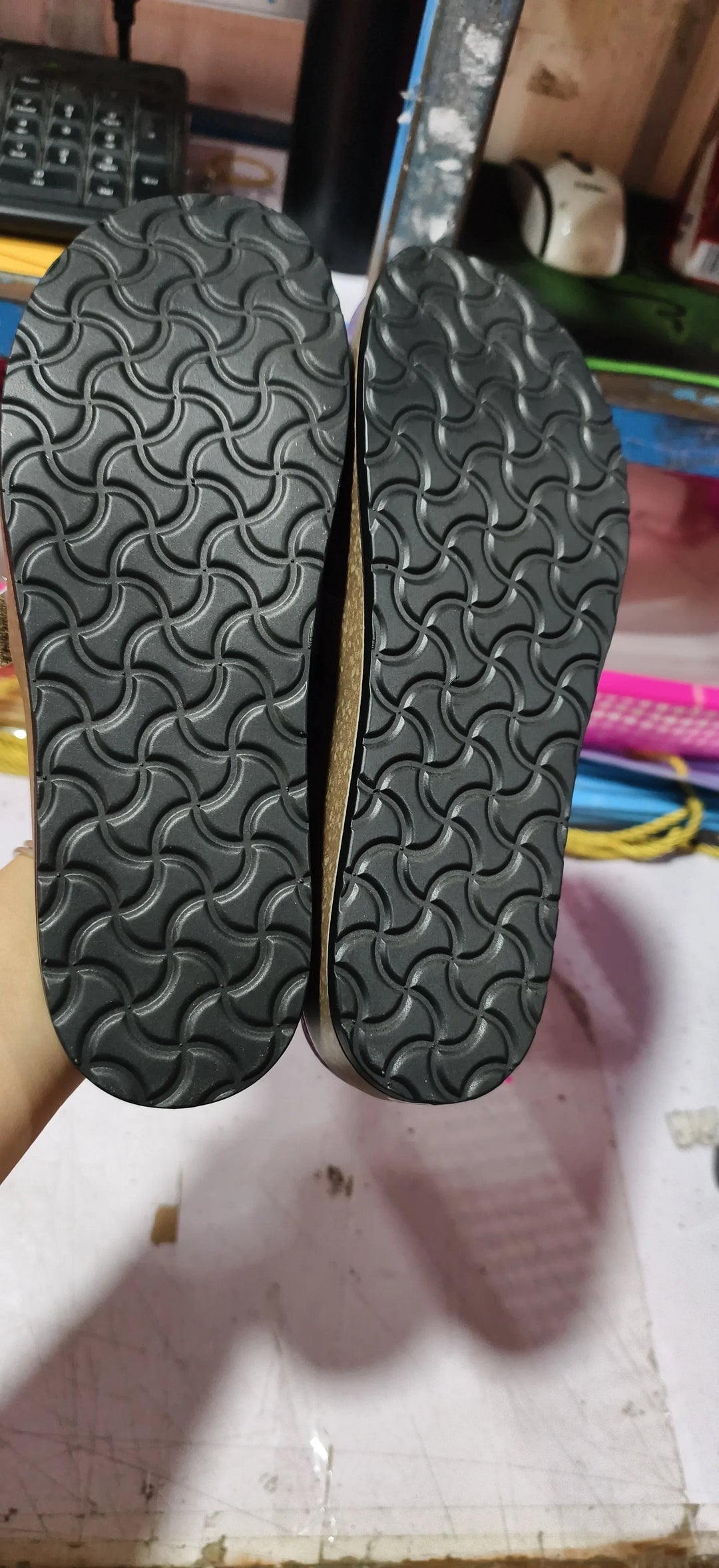 Close-up of black sandal soles with textured geometric patterns held against a cluttered background