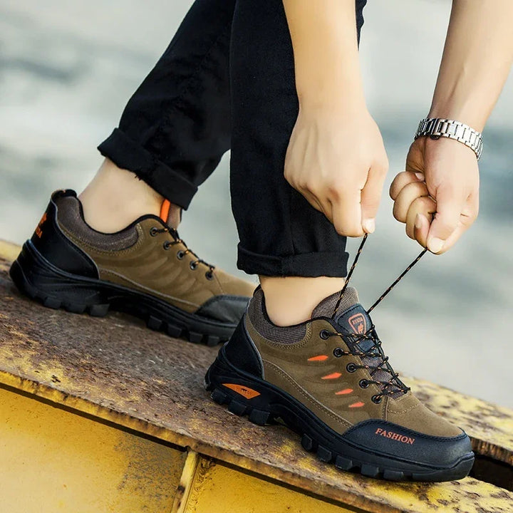 Person tying laces on brown and black durable outdoor hiking shoes with orange details