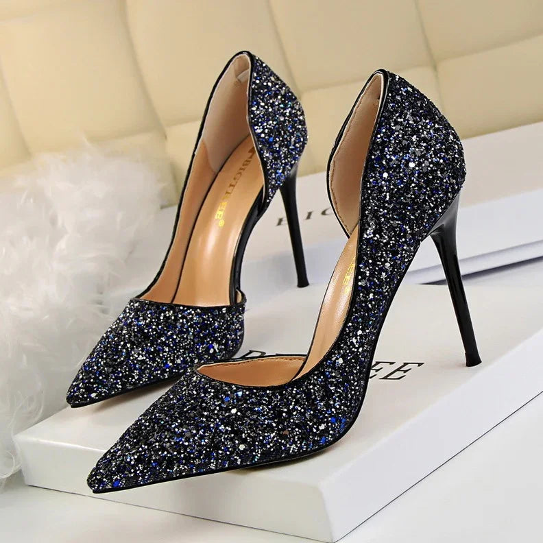 Pair of black glitter stiletto high heels with pointed toes on a white box