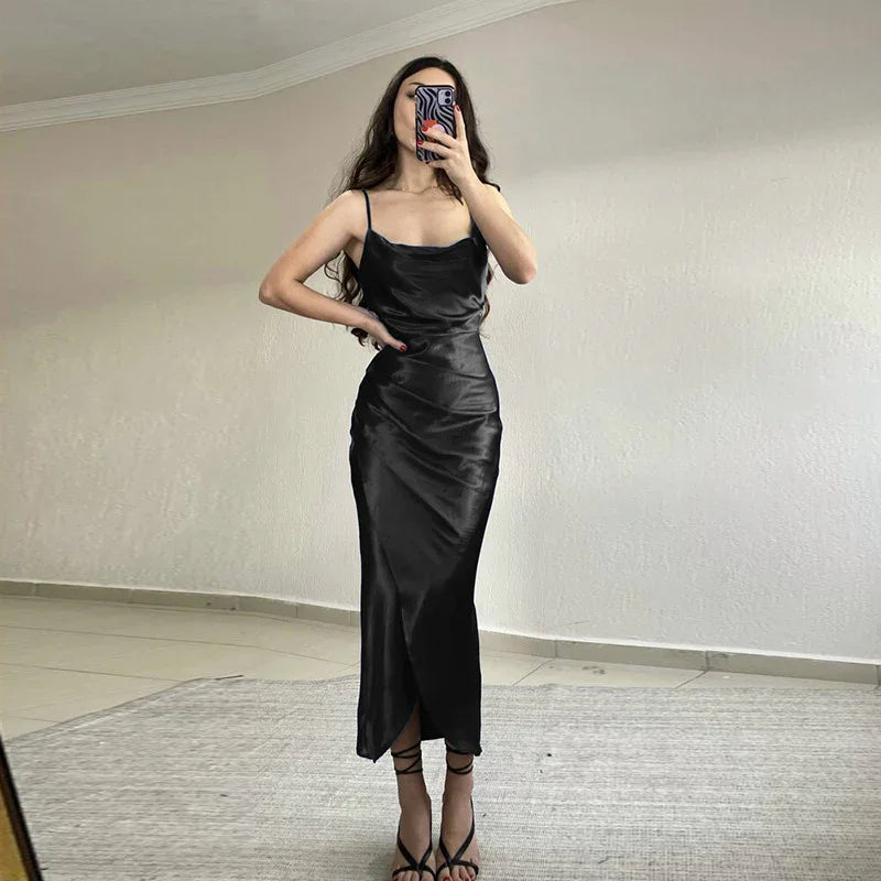 Woman in black satin slip dress with spaghetti straps taking mirror selfie indoors on gray rug