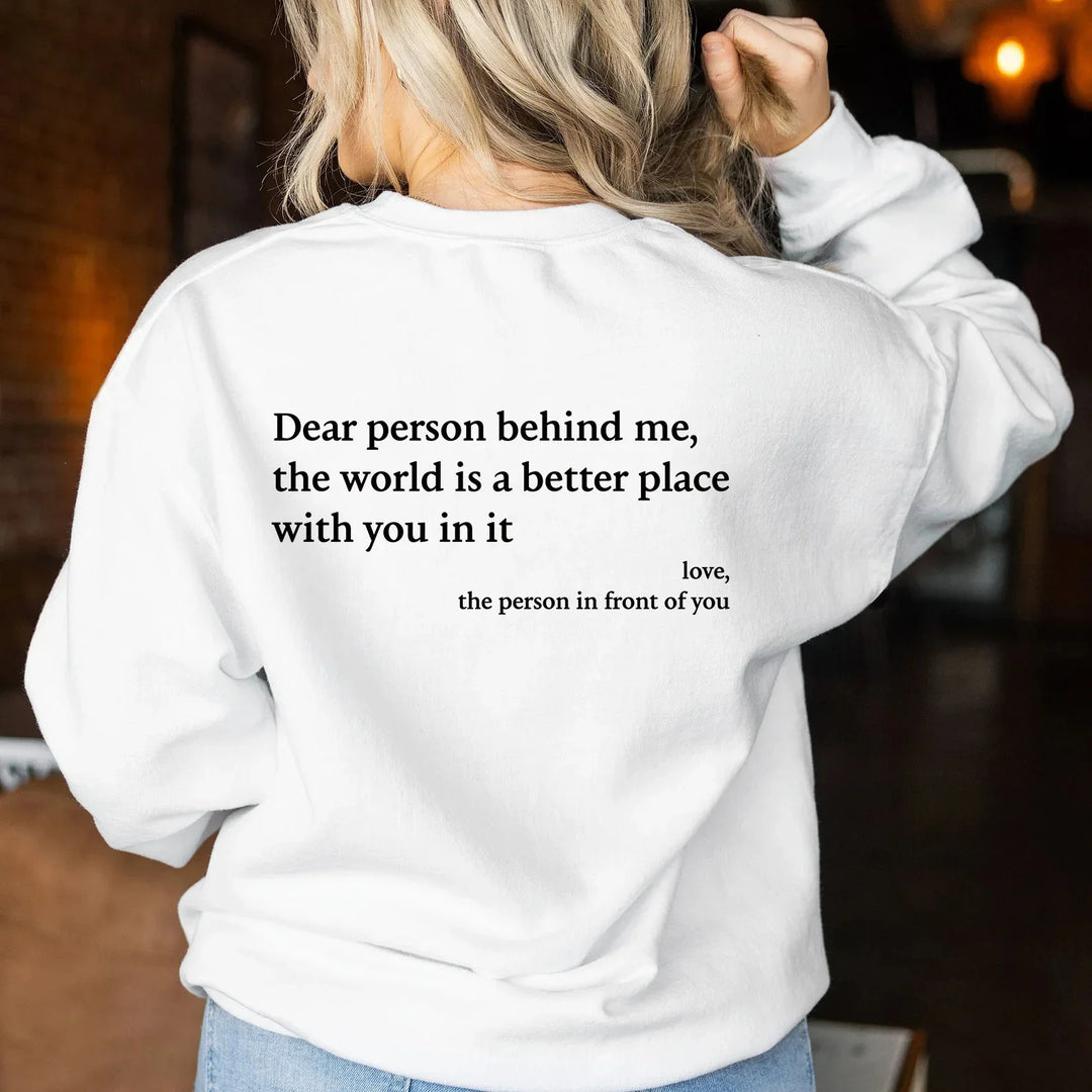 Blonde woman wearing white sweatshirt with uplifting quote on back in a cozy indoor setting