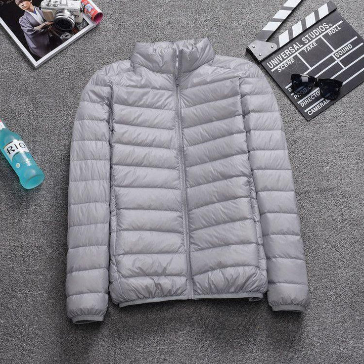 Light gray quilted puffer jacket laid flat on gray carpet with magazine, drink bottle, clapperboard, and sunglasses nearby