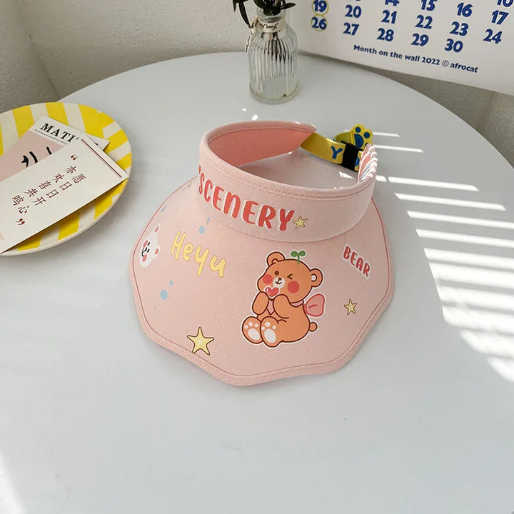 Pink sun visor hat with cute bear, text 'SCENERY', 'Heyu', and star decals on white table