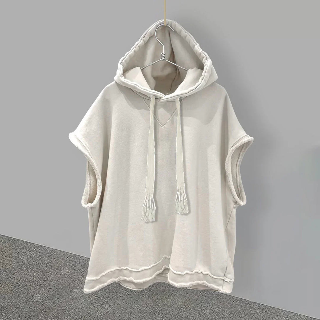 Light beige sleeveless hoodie with drawstrings hanging on a metal hanger against gray background