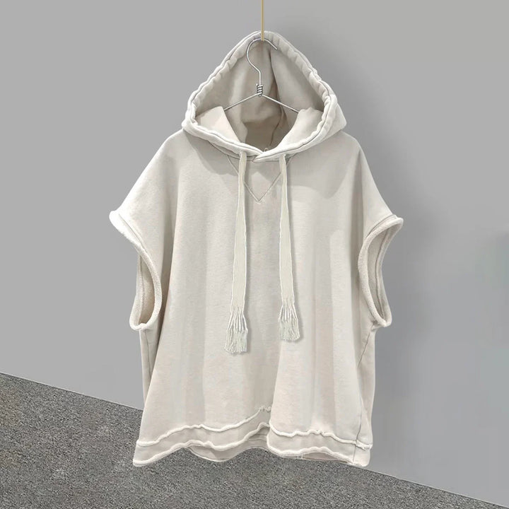Light beige sleeveless hoodie with drawstrings hanging on a metal hanger against gray background
