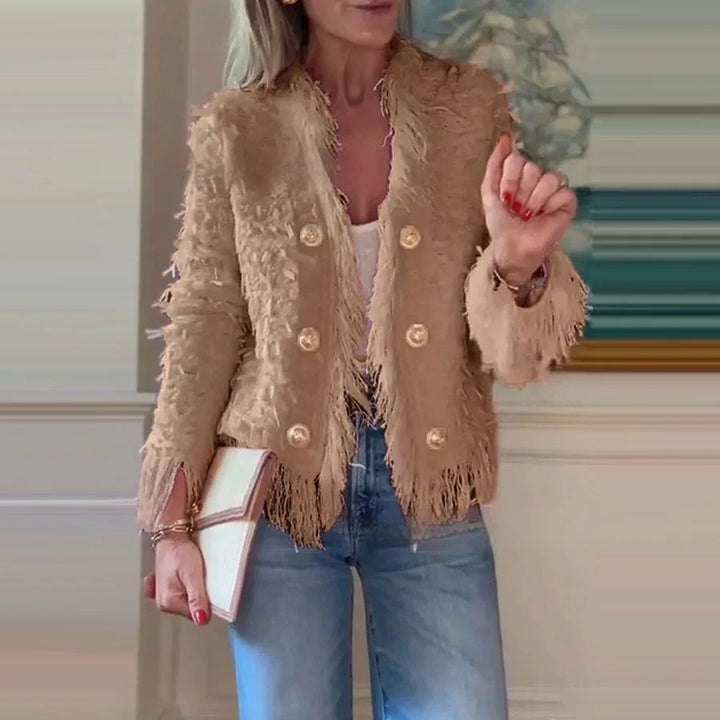 Woman wearing beige textured fringe blazer with gold buttons, blue jeans, white top, holding clutch