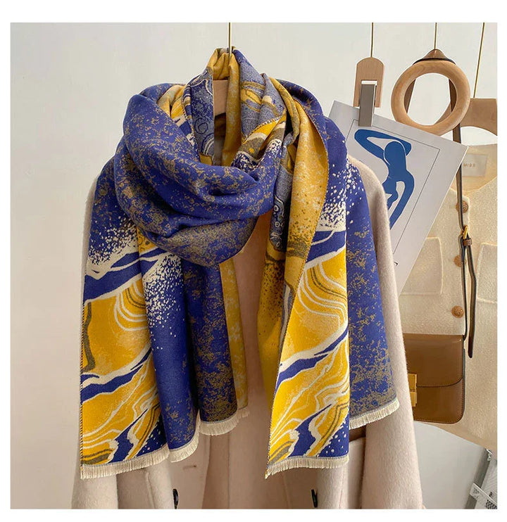 Soft wool blend scarf with blue, yellow, and white abstract pattern draped over beige coat on hanger