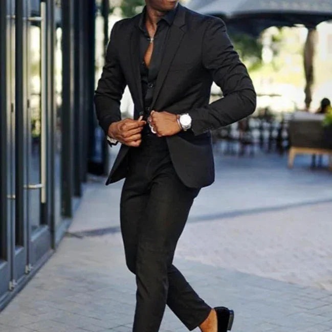 Man in a fitted black suit and dress shoes walking outdoors by glass building in stylish urban setting