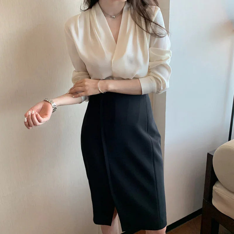 Woman wearing cream satin blouse and high-waisted black pencil skirt in modern indoor setting