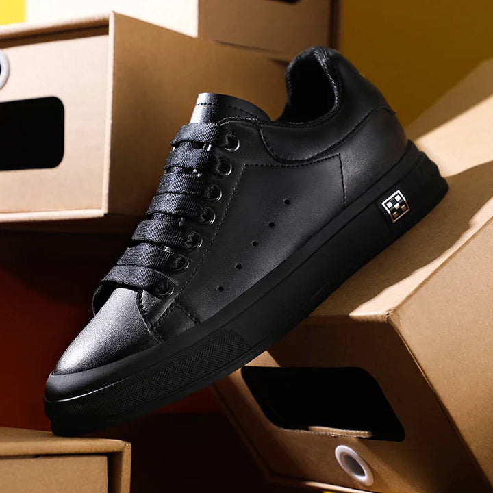 Black leather low-top sneaker with black laces and logo detail on sole, displayed on stacked cardboard shoe boxes